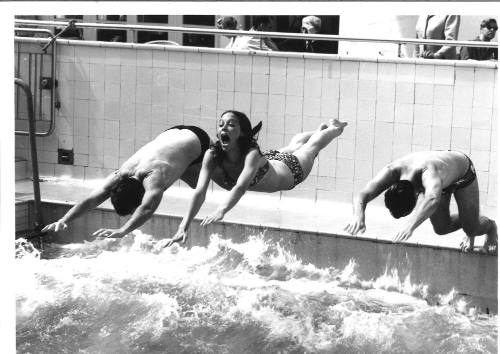 Photograph depicting three people diving into a pool