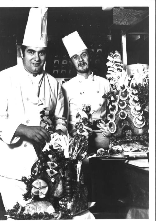 Photograph depicting two chefs posing next to a food display