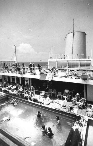 Photograph depicting passengers sunbathing by the edge of the ship's pool