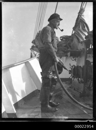 Boatswain Karl Muller smoking a pipe and hosing the deck of SEETEUFEL