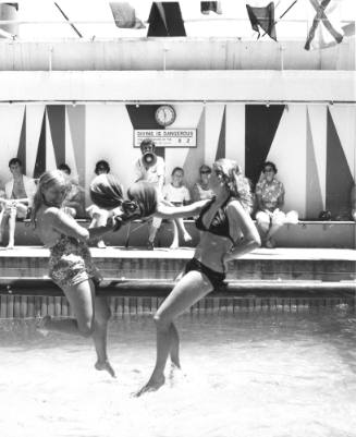 Photograph depicting two women on the greasy pole over the ship's pool