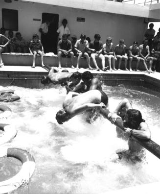 Photograph depicting seven men climbing on the greasy pole