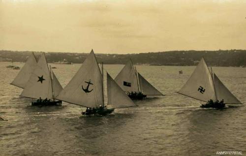 Postcard featuring a photograph of five skiffs sailing on the water, with land in the background, each sail displays a different symbol or flag