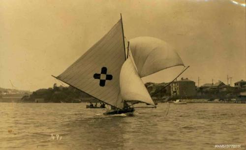 Postcard featuring a photograph of skiff sailing in the water, with land and houses visible behind it