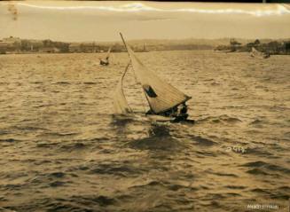 Black and white photograph of three skiffs sailing, with land and buildings visible in the background