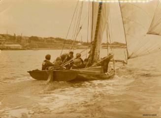 Black and white photograph showing several men sitting in a skiff, which is sailing close to land
