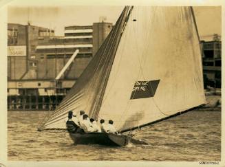 Skiff sailing in the water, with several crew members