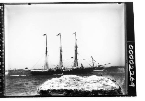 Three masted schooner on an unknown harbour with a dark stretch of land across the background