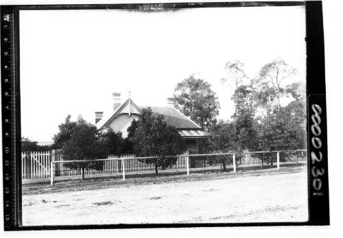 Single storey house behind a white picket fence viewed from the road