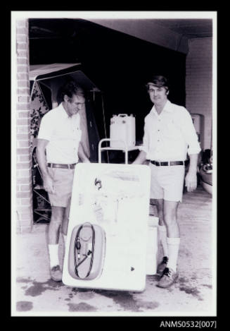 Two men facing camera with rectangular object marked Johnson 6'