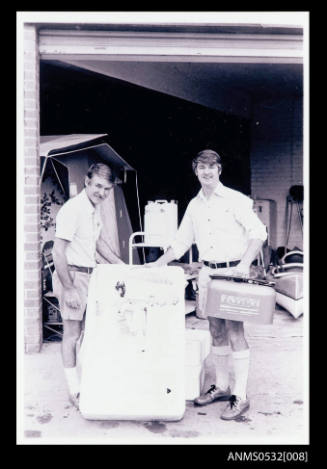 Two men facing camera with rectangular object marked Johnson 6'