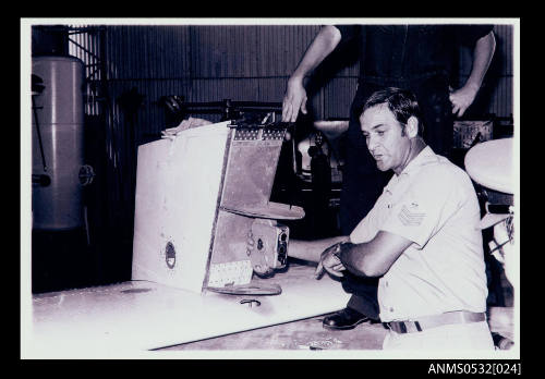 Scene in large room at lower left corner and bottom centre is metallic object [part of SPIRIT OF AUSTRALIA] with box like object attached at lower centre