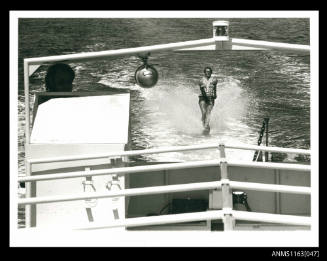 The large power boat, looking aft at a man being towed on single water ski