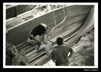 The man inside a fibre glass boat hull, fitting timber strengthening pieces to the keel