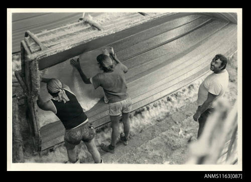 The view of two men placing fibreglass matting in stern area on fibreglass boat