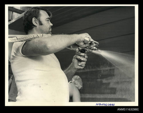 The view of man spraying epoxy resin into the fibreglass hull of boat under construction