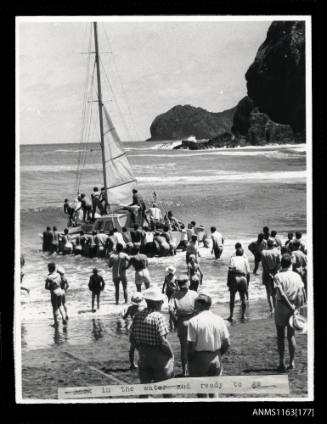 The single masted trimaran with cabin being pushed out to sea by many people