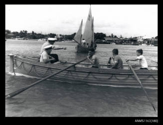 Boys and men rowing life boat and sailing vessel marked RAN 33