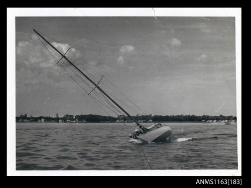 The a single masted sailing boat, sails furled, almost on its starboard side, which appears to be supported by some form of pontoon