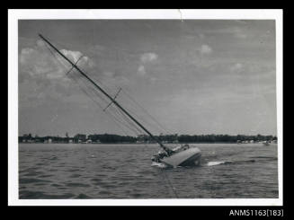 The a single masted sailing boat, sails furled, almost on its starboard side, which appears to be supported by some form of pontoon