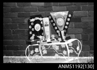 Black and white negative number 31A depicting display of boating trophies on a wrought iron table at state sports, pleasure outboard championships, Cabarita, Parramatta River, Sydney, New South Wales