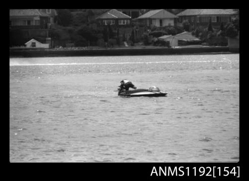 Black and white negative number 18 depicting power boat stationary midstream with driver inspecting outboard engine