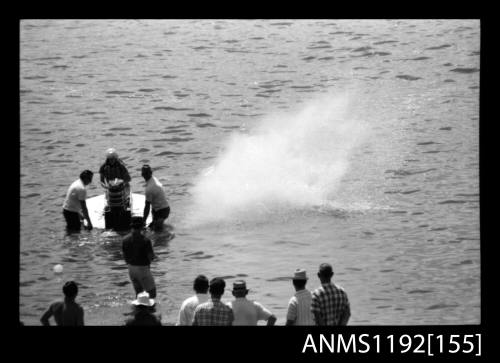 Black and white negative number 19 depicting power boat stationary with engine running and two men holding the boat still