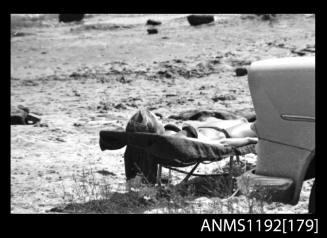 Black and white negative number 12 depicting spectator on camp bed near parked car at Outboard Engined Hydroplane titles, Cabarita, Parramatta River, Sydney