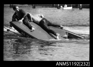 Black and white negative number 4 depicting He15n Power boat, under tow with stern section under water, two men lying on raised fore deck