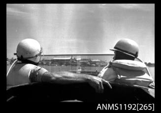 Black and white negative number 15 depicting view of open power boat with back of the heads of two men seated near windscreen