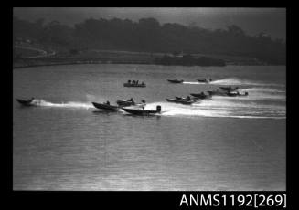 Black and white negative number 12A depicting view of 13 open power boats at speed most with outboard engine