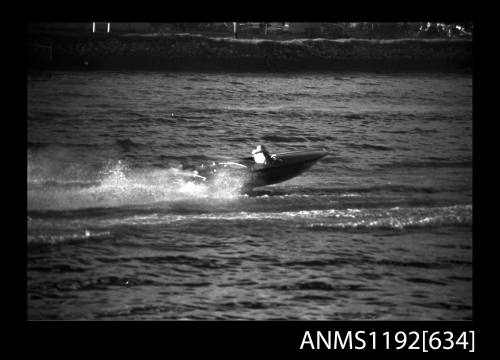 Black and white negative number 16A depicting view of power boat completing a turn and almost hidden by spray, starboard side view