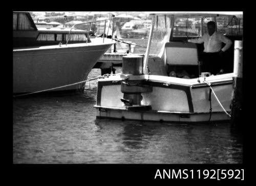 Black and white negative number 15 depicting view of boiler mounted outboard on transome of motor cruiser, stern/ starboard side view, from jetty / boat