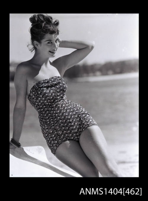 Photographic negative of swimsuit model leaning on an over turned boat