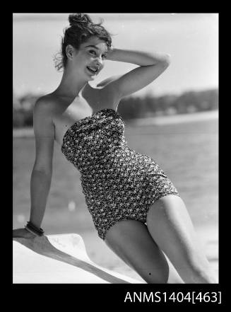 Photographic negative of swimsuit model leaning on an over turned boat