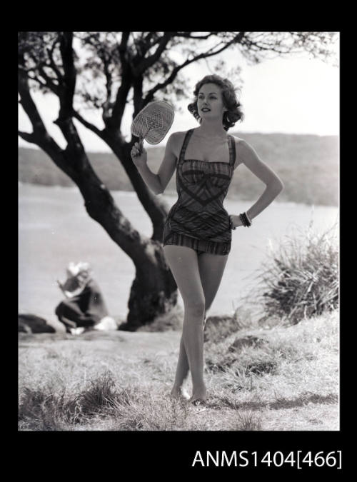 Photographic negative of swimsuit model  posing on a grassy hill, overlooking a cove