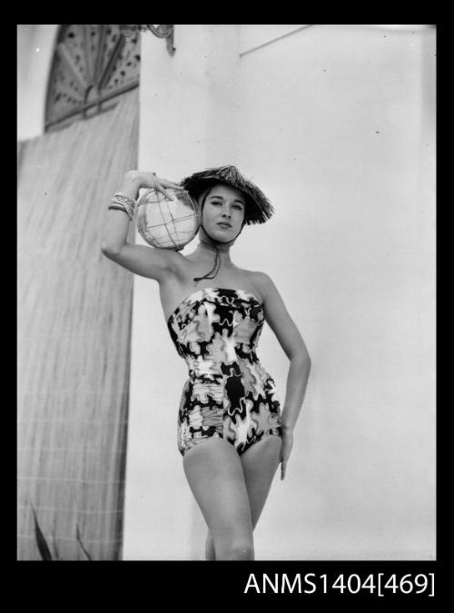 Photographic negative of swimsuit model posing with a straw hat and large glass orb