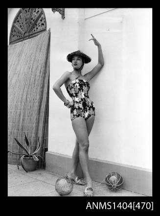 Photographic negative of swimsuit model posing with a straw hat and two glass orbs