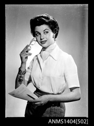 Photographic negative of a model posing with reading glass and paper