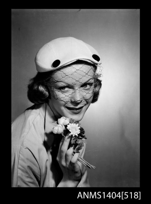 Photographic negative of a model posing with a hat and small posy of flowers