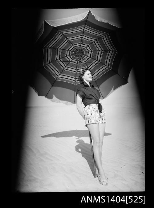 Photographic negative of a model posing in casual wear with large umbrella