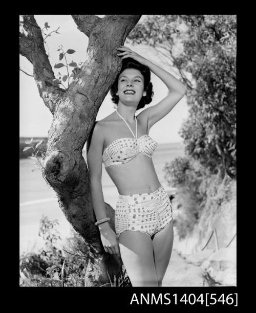 Photographic negative of a swimsuit model posing with a tree near a beach