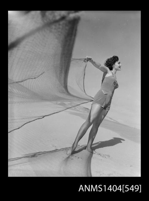 Photographic negative of a swimsuit model posing on a beach with a fishing net