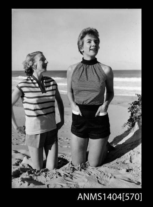 Photographic negative of two models in casual wear posing on a beach