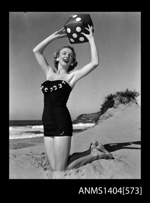 Photographic negative of a swimsuit model posing on a beach with a blow-up dice