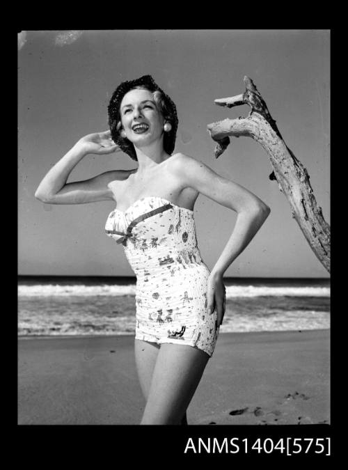 Photographic negative of a swimsuit model posing on a beach in a hat