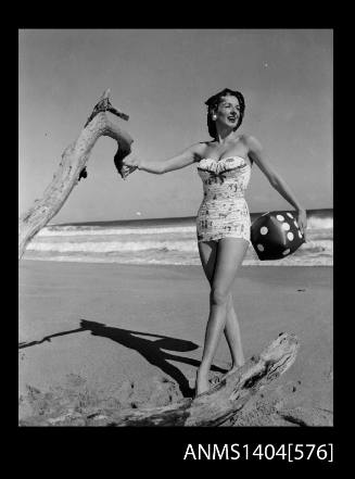 Photographic negative of a swimsuit model posing on a beach holding a blow-up dice