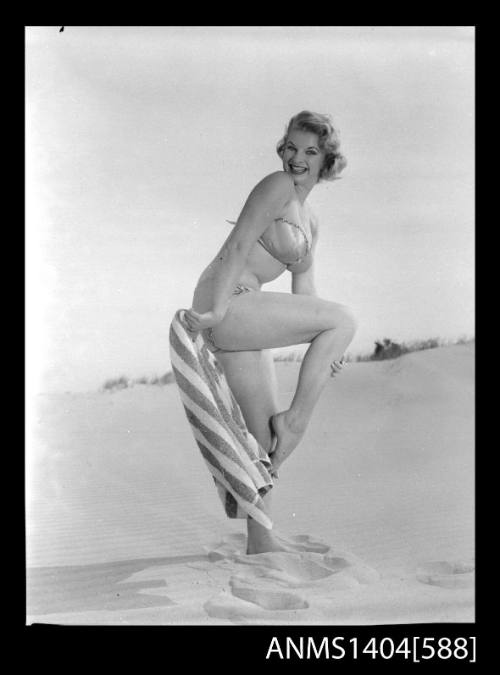 Photographic negative of a swimsuit model posing with a towel on a sand dune