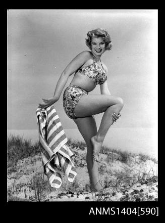 Photographic negative of a swimsuit model posing with a towel on a sand dune