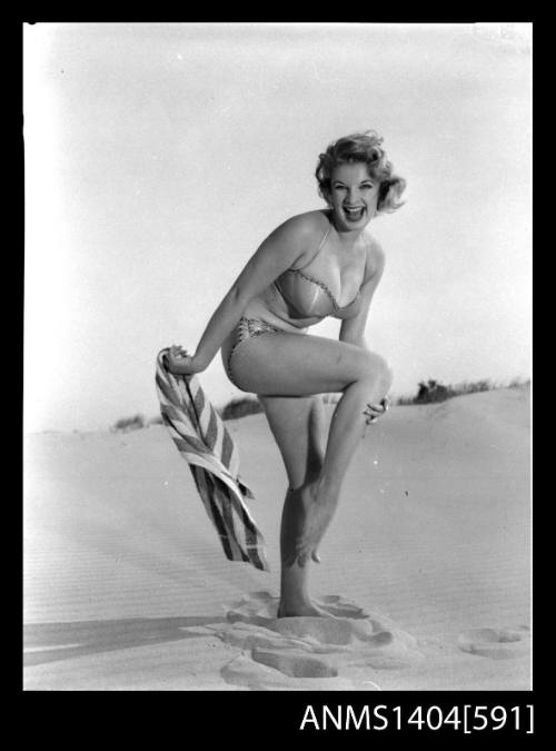 Photographic negative of a swimsuit model posing with a towel on a sand dune